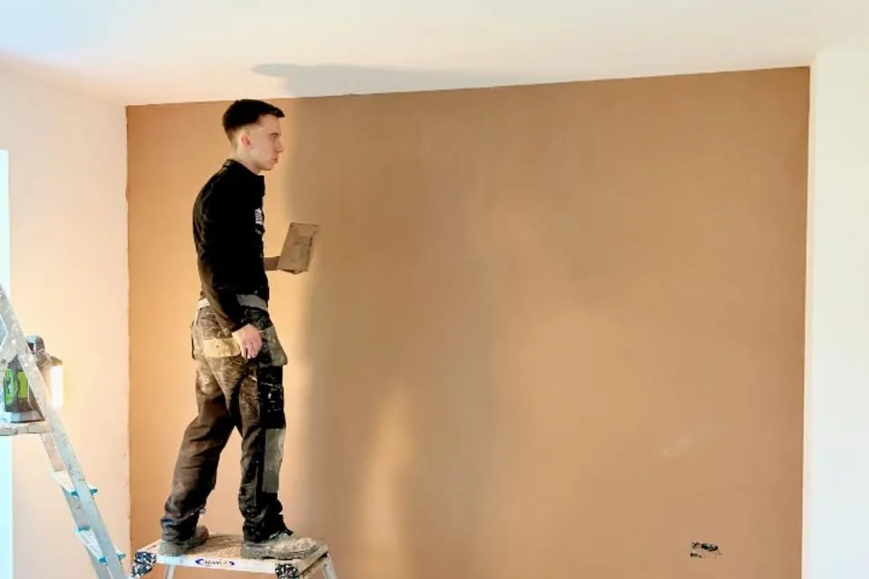 Plastering a living room wall from a hop-up, with the floor sheeted