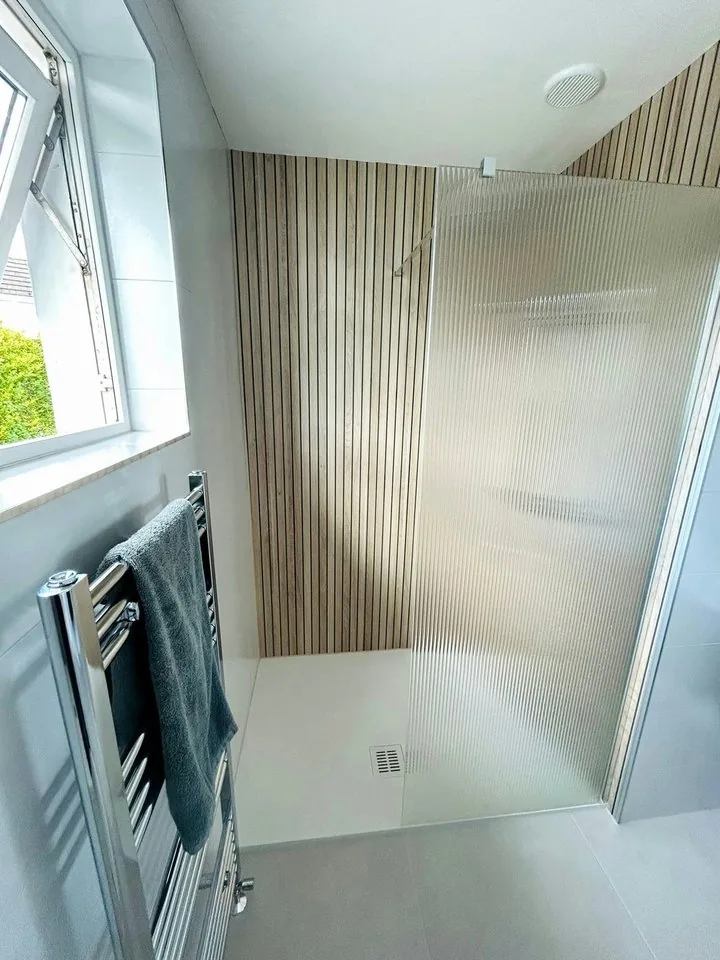 Walk-in shower with slatted panels beside a heated towel rail