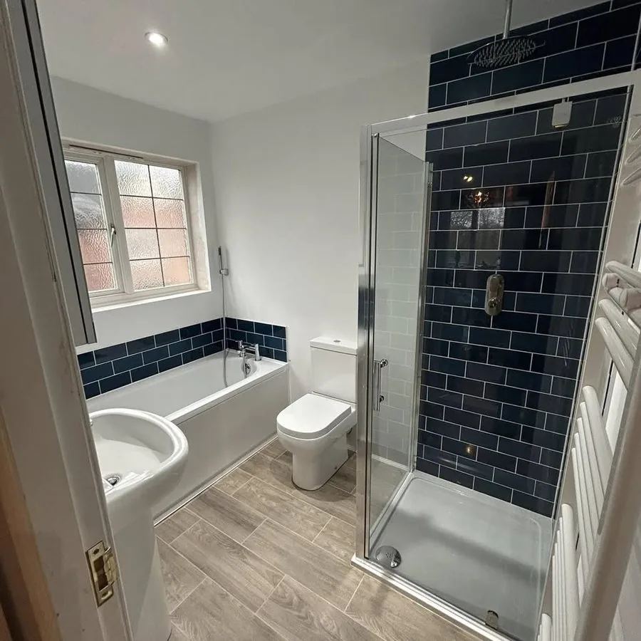 After: the same bathroom with a new bath, walk-in shower and navy tiles